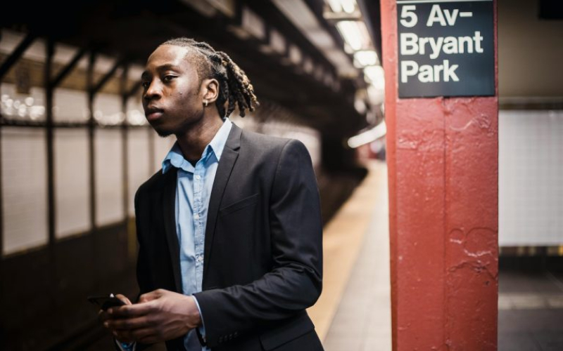 Person in a suit standing on a subway platform near a sign for 5th Ave-Bryant Park station.