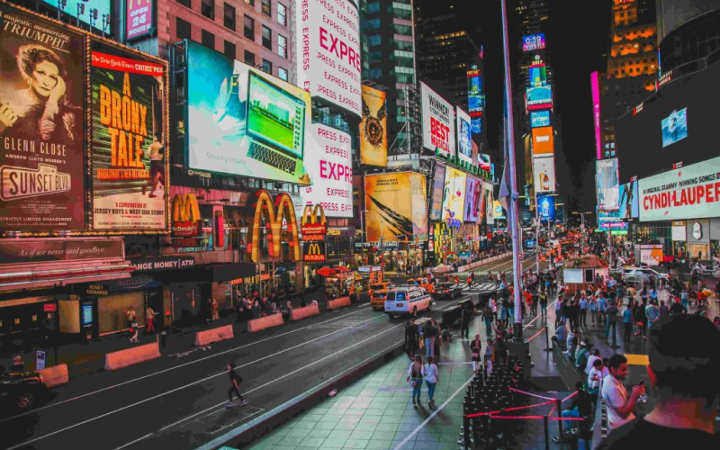Brightly lit Times Square at night with busy streets, billboards, and crowds of people.