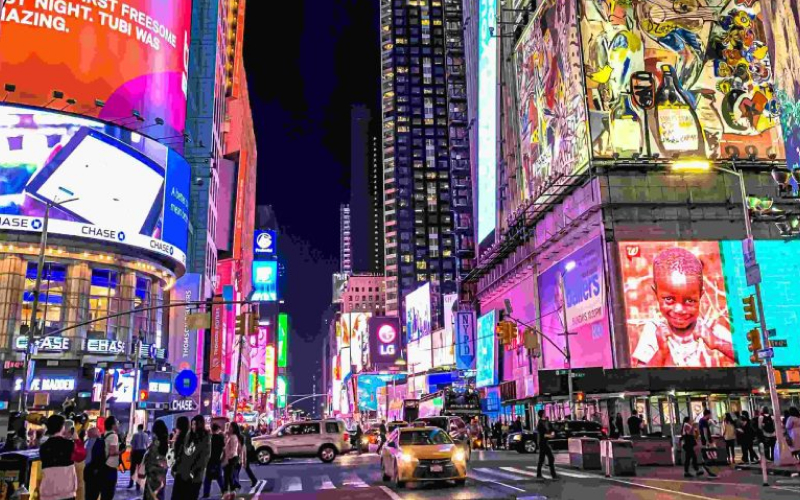 A vibrant, neon-lit city street bustling with people and cars at night, showcasing colorful billboards.