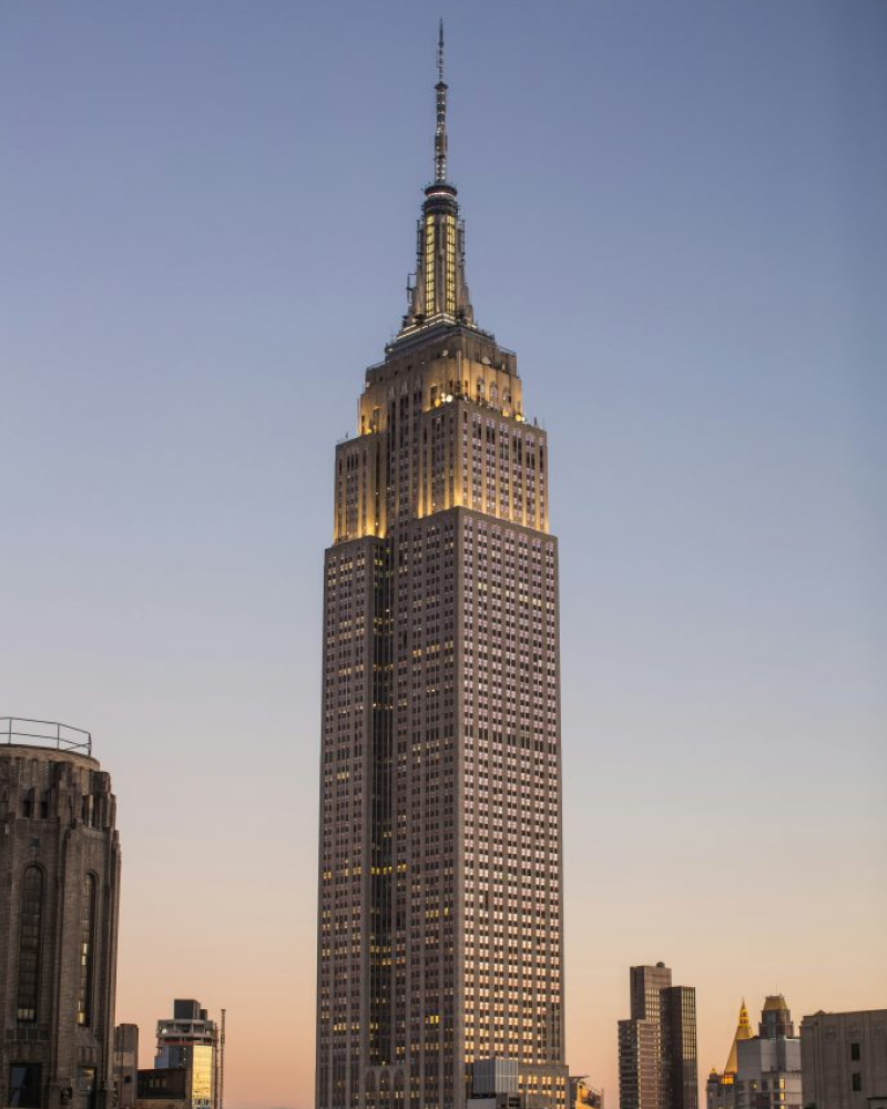 A tall skyscraper with illuminated windows against a clear evening sky.