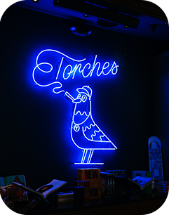 Blue neon sign of a bird holding a torch with the word Torches above it, on a dark wall.
