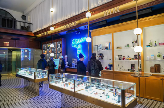 People browsing in a modern store with display cases, neon signs, and labeled shelves saying STIMULATE and RELAX.