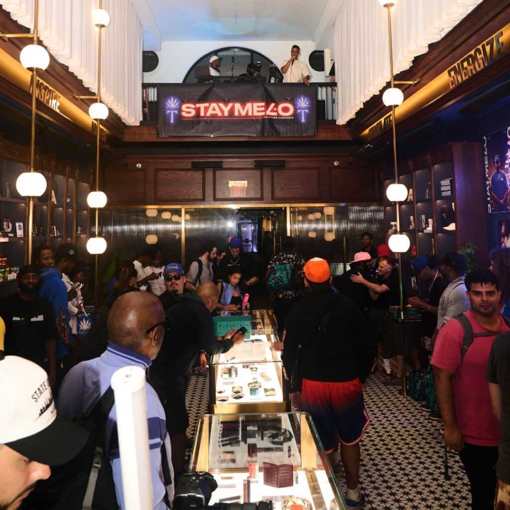 A bustling store with glass display cases, shoppers exploring every corner, and a prominent STAYME7O sign shining above from the balcony.