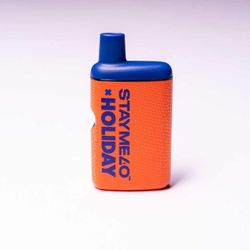 Small orange and blue vape device labeled STAYME40 HOLIDAY and STAYME7O, set against a light purple background.