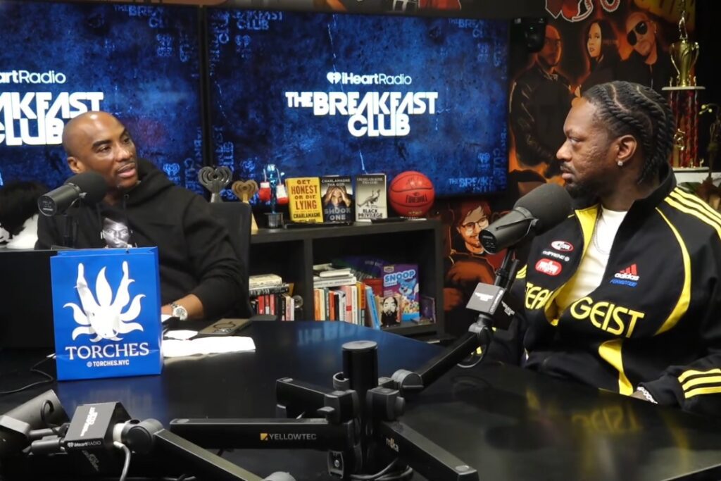 Two men have a conversation in a radio studio, with The Breakfast Club Cast logo visible in the background.